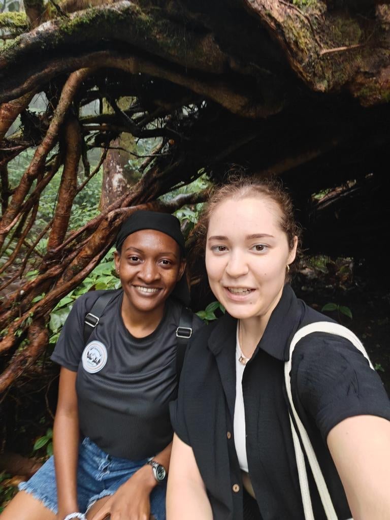 Two young women smiling at the camera under gnarled tree branches with moss and green foliage