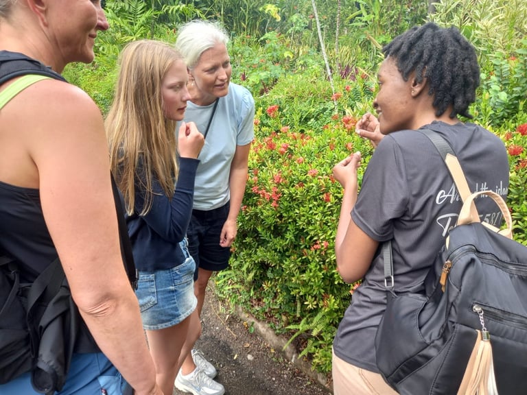 Four people in casual clothing having a conversation outdoors in front of green foliage and red flowers