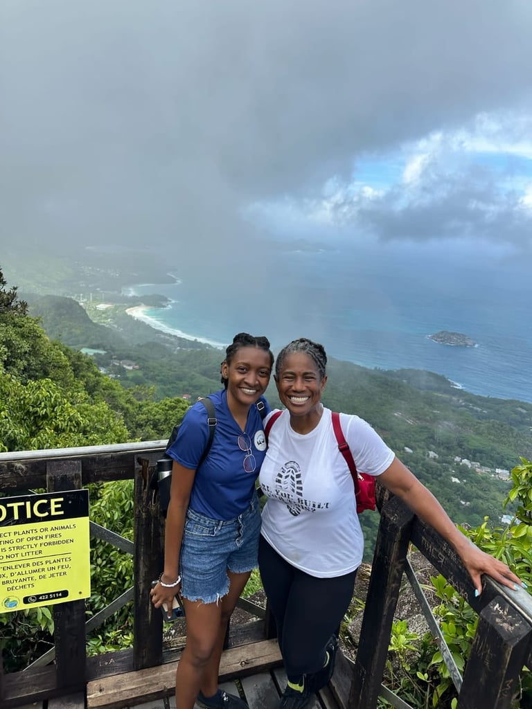 Two women smiling at scenic mountain overlook with coastal view and cloudy sky in background
