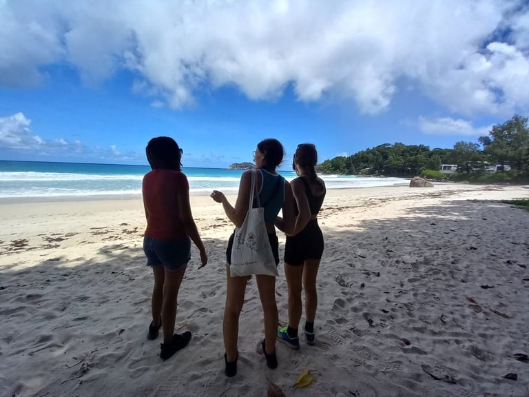 Three people standing on a sandy beach facing the ocean under a blue sky with white clouds
