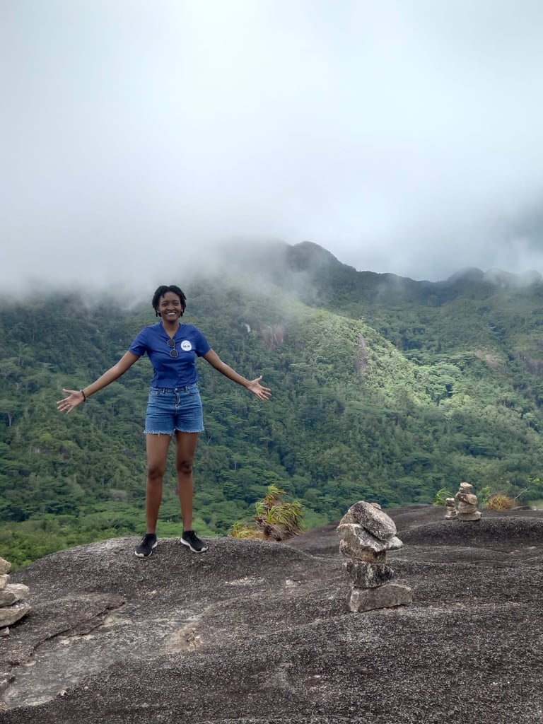 Man in blue athletic wear standing with arms spread wide on a rocky outcrop overlooking lush green forested mountains shrouded in mist