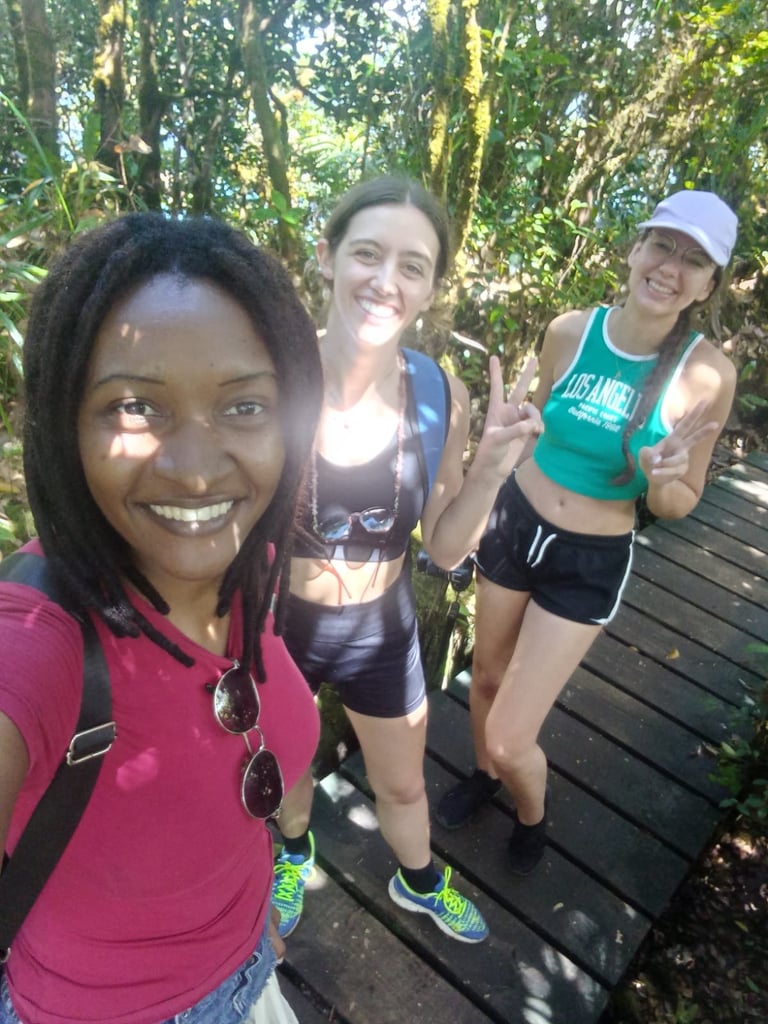 Three women smiling on a wooden trail surrounded by lush green forest canopy