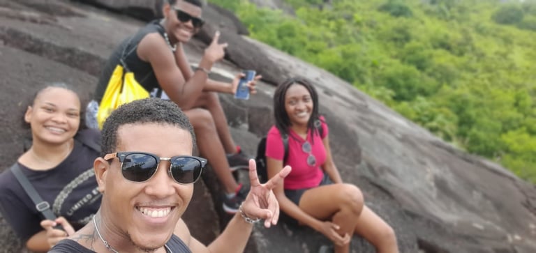 Group of people smiling and posing together on a rocky hillside with green forest in the background