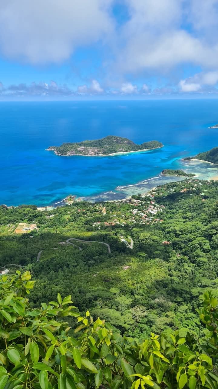 Aerial view of a tropical island surrounded by turquoise ocean, lush green coastline, and winding mountain road