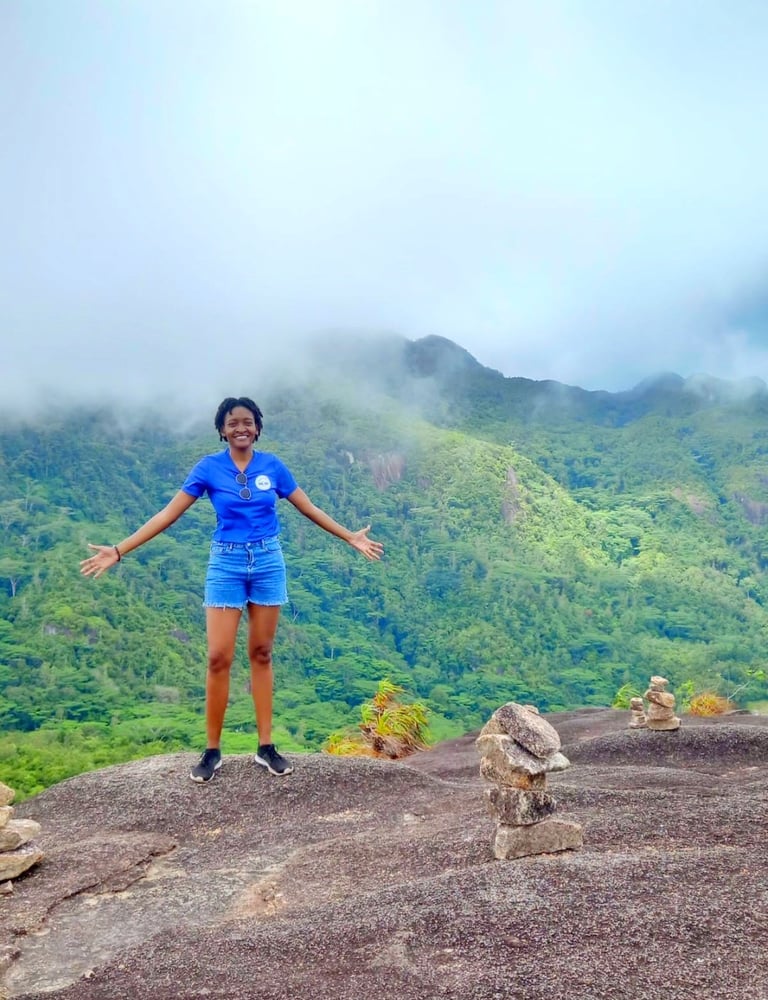 Woman in blue athletic wear standing with arms outstretched on rocky outcrop overlooking lush green mountains