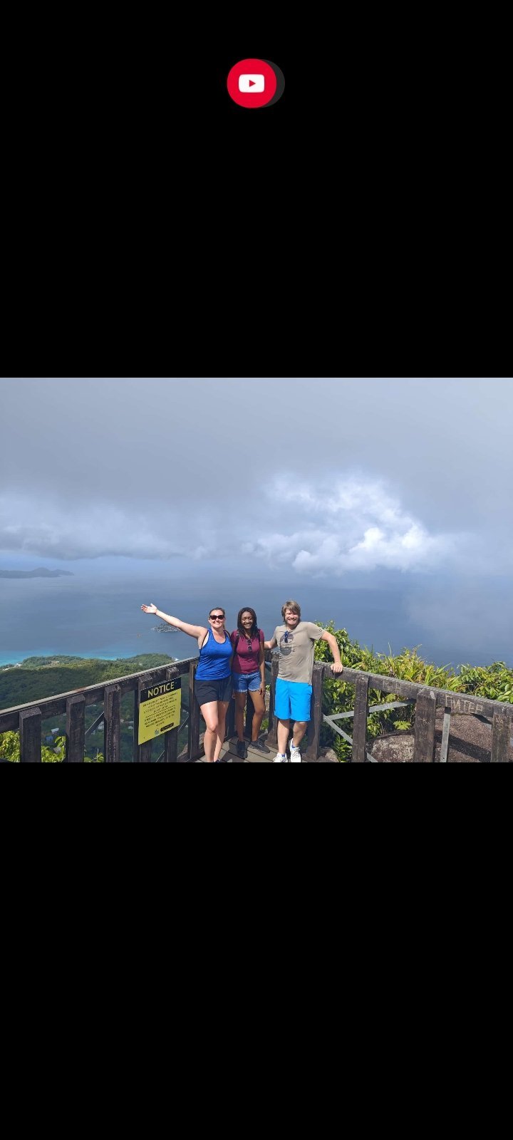 Four people posing on a scenic overlook with ocean and cloudy sky in background
